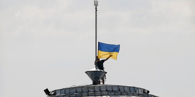 A climber installs the Ukrainian national flag on a roof, marking the Day of the State Flag, on the eve of the Independence Day, in Kiev, Ukraine, Aug. 23, 2016. (REUTERS/Gleb Garanich)