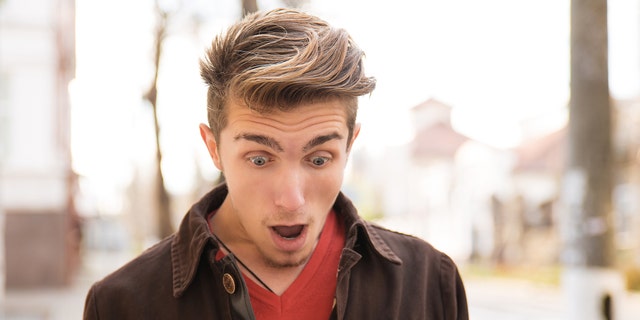 Young shocked man receiving news on smartphone and looking shocked while standing on street