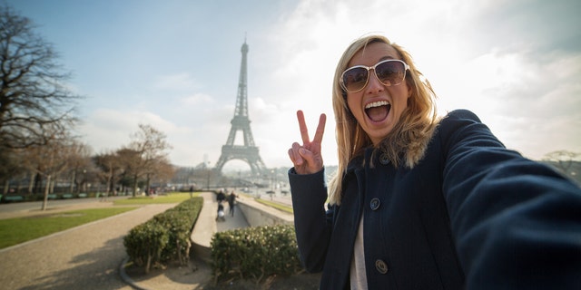 Woman takes selfie in front of the Eiffel Tower in Paris, France.