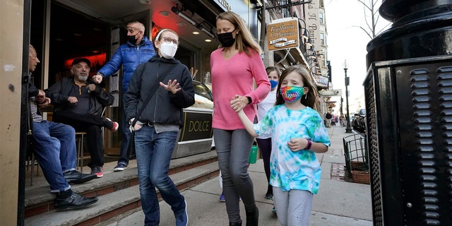 People walking down the street are shown wearing masks against COVID-19.
