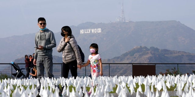 Visitors walk past a memorial for victims of COVID-19 at the Griffith Observatory, on Friday, Nov. 19, 2021, in Los Angeles. Thousands of flags were placed on the lawn in front of the observatory in memory of those who have died of COVID-19 in Los Angeles County as of Nov. 2. 