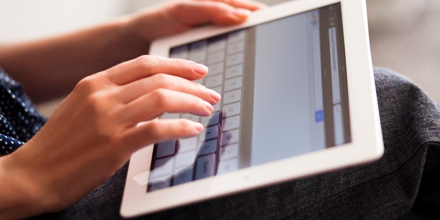 Woman hands printing on iPad keyboard in Google search.