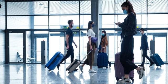 People traveling by plane during the coronavirus pandemic are shown wearing face masks as they walk through an airport terminal. 