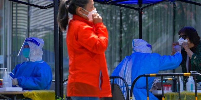 Resident gets a throat swabbed during a mass COVID test set up outside a shuttered commercial office complex on Tuesday, May 17, 2022, in Beijing.