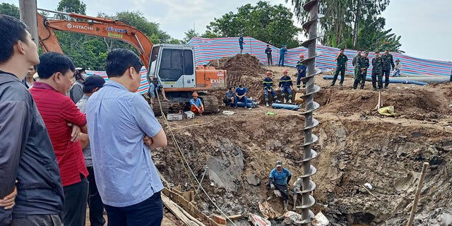 Rescuers look down into the site of where a 10-year-old boy is thought to be trapped in a 35-metre deep shaft at a bridge construction area in Vietnam's Dong Thap province on January 2, 2023.