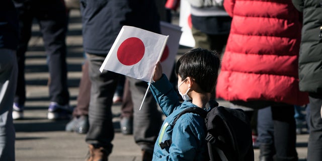 A boy holds a Japanese national flag during the New Year's appearance by the Japanese royal family at the Imperial Palace on January 2, 2023, in Tokyo, Japan.