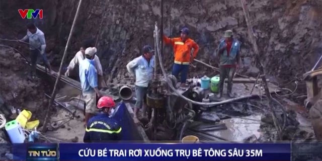 Various rescuers and construction workers dig around concrete hole to save boy.